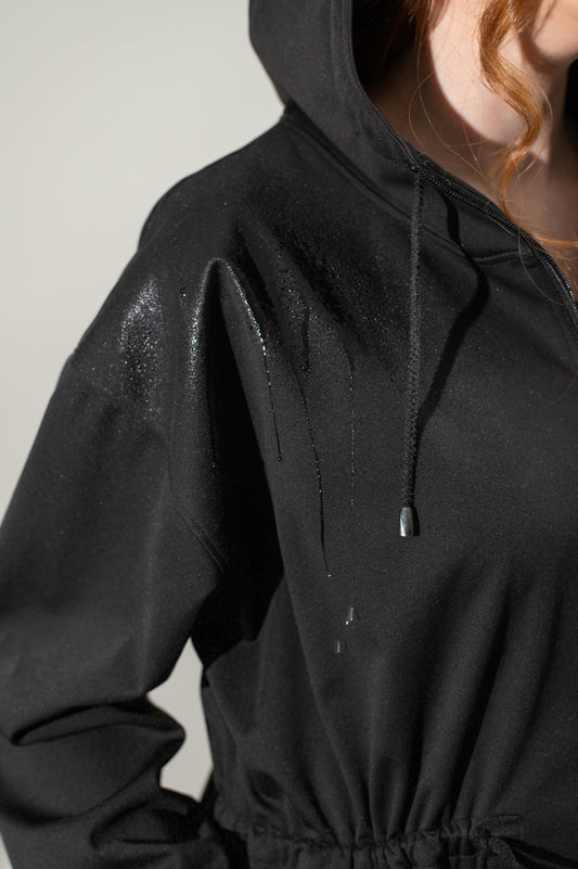 Black hooded jacket with water droplets on a plain background