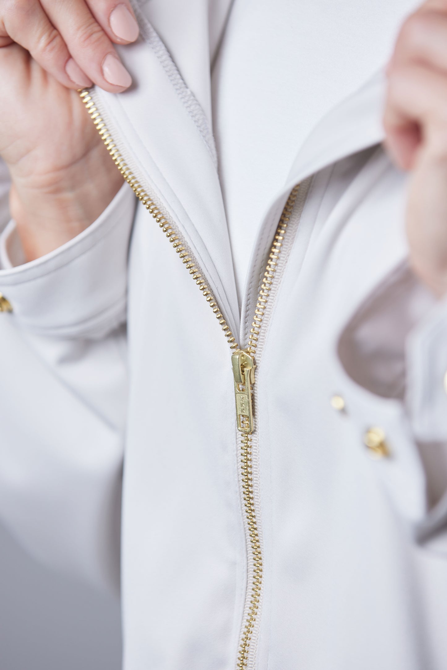 Close-up of a person zipping up a white jacket with a gold zipper.