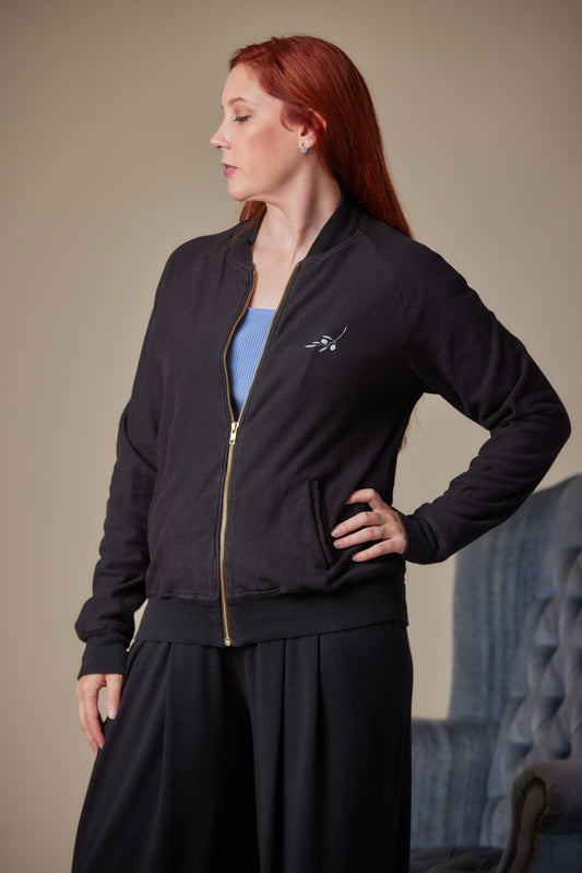 Woman wearing a black jacket with a gold zipper against a neutral background