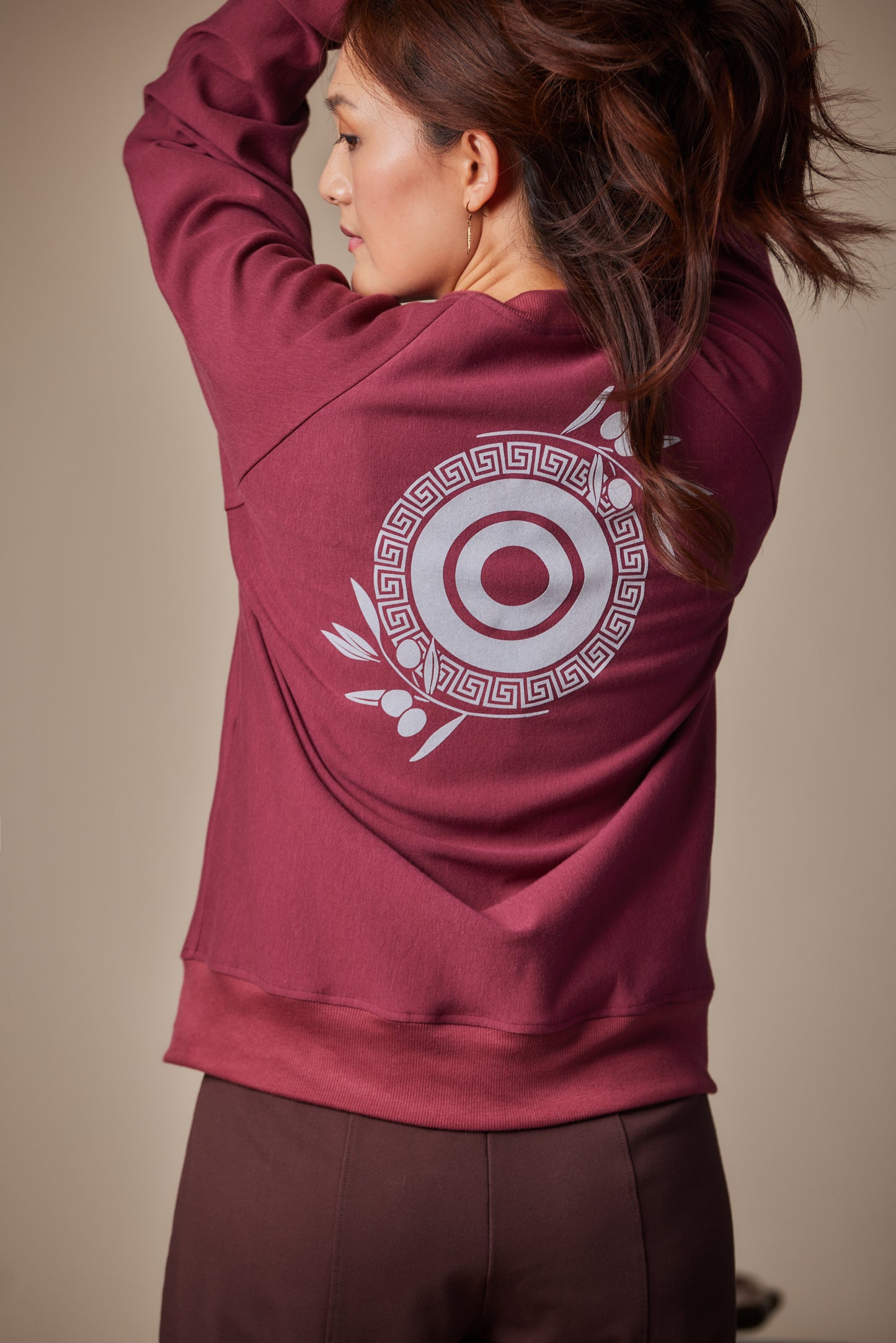 Person wearing a maroon hoodie with a white circular design on the back against a beige background