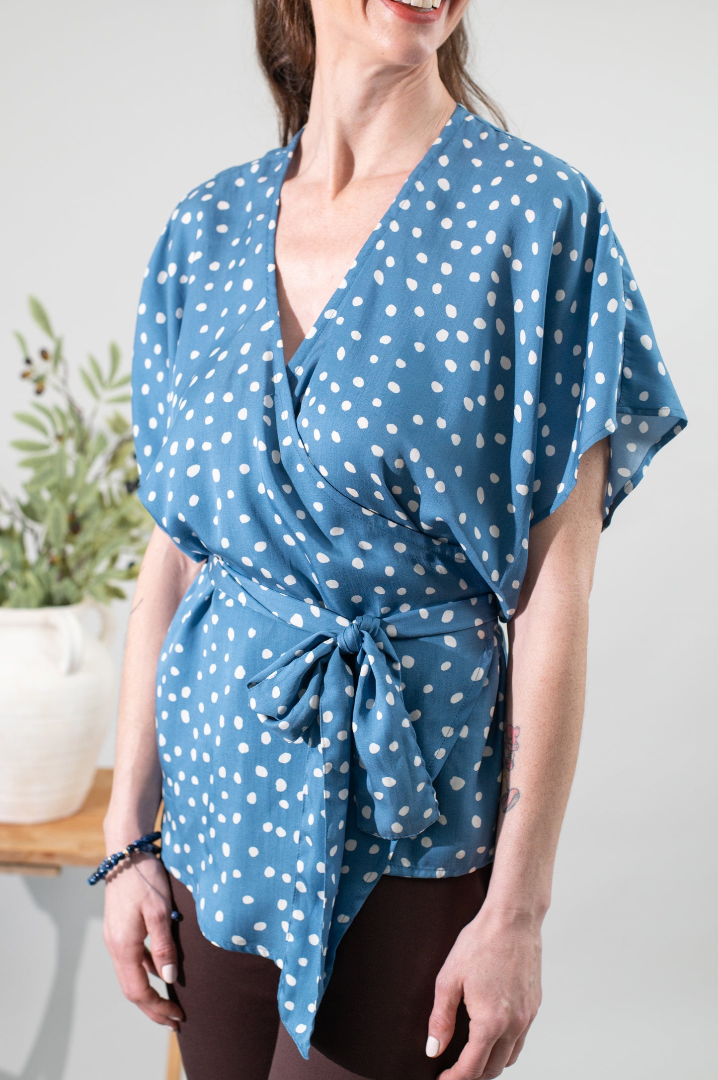 Woman wearing a blue polka dot wrap top against a white background