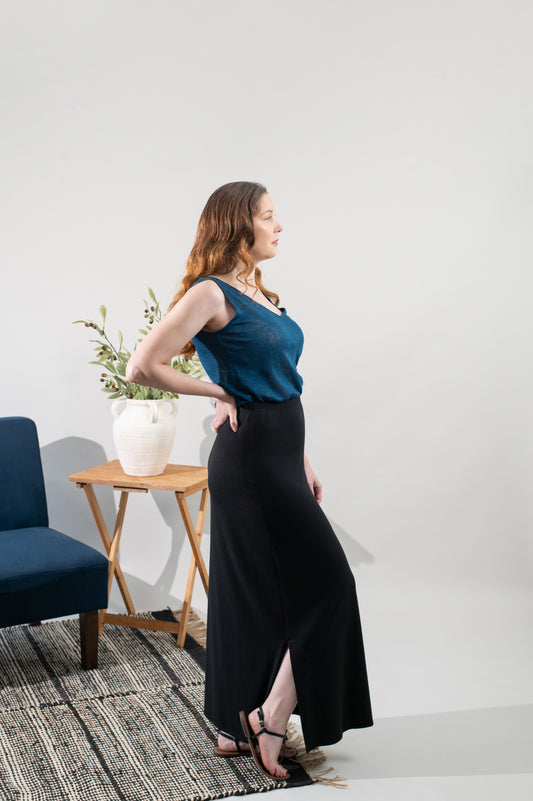 Woman in a blue top and black skirt standing in a room with a couch and plant.