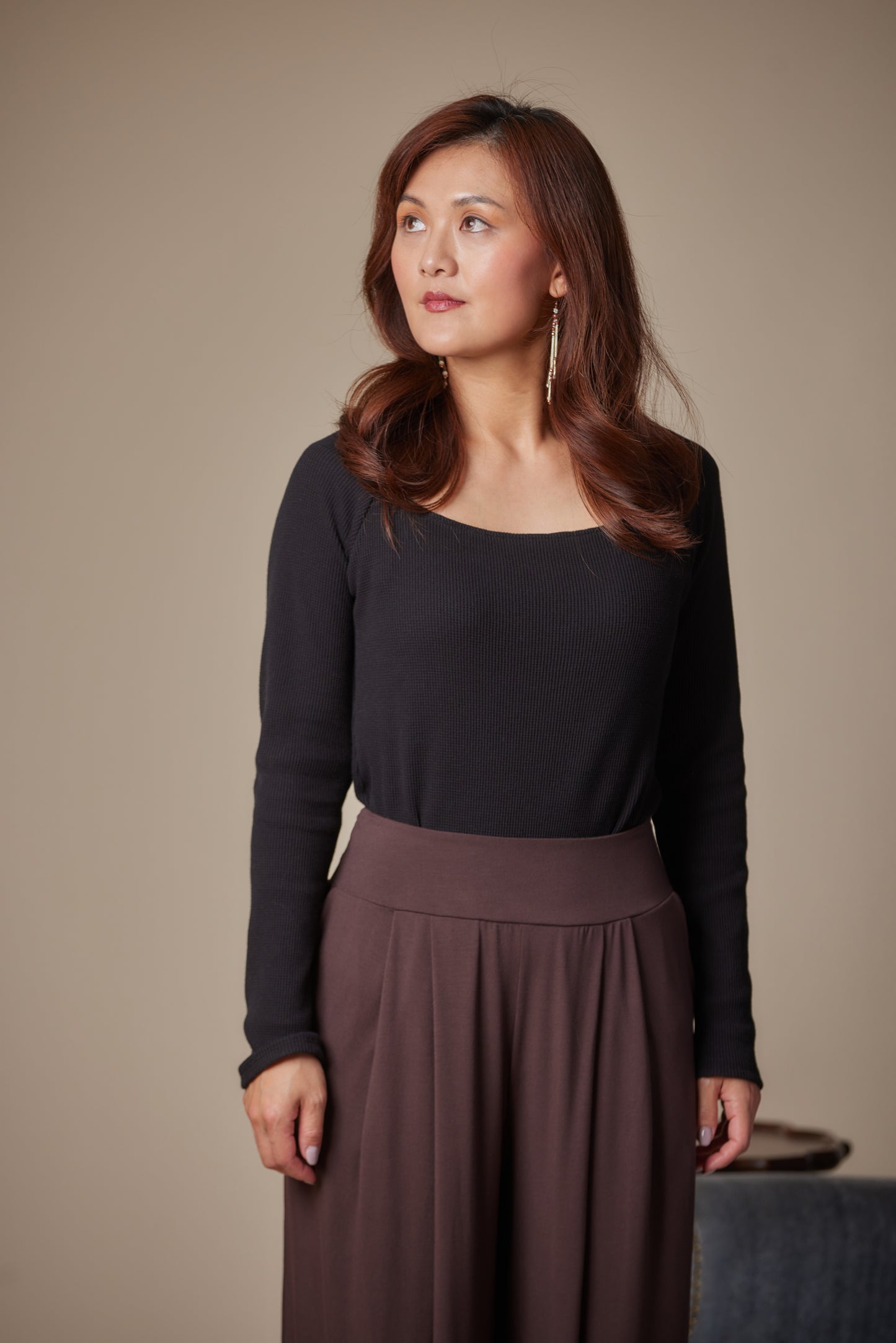 Woman wearing a black top and brown skirt against a beige background