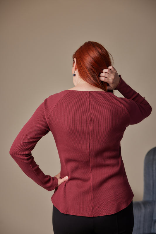 Person wearing a burgundy long-sleeve top against a beige background