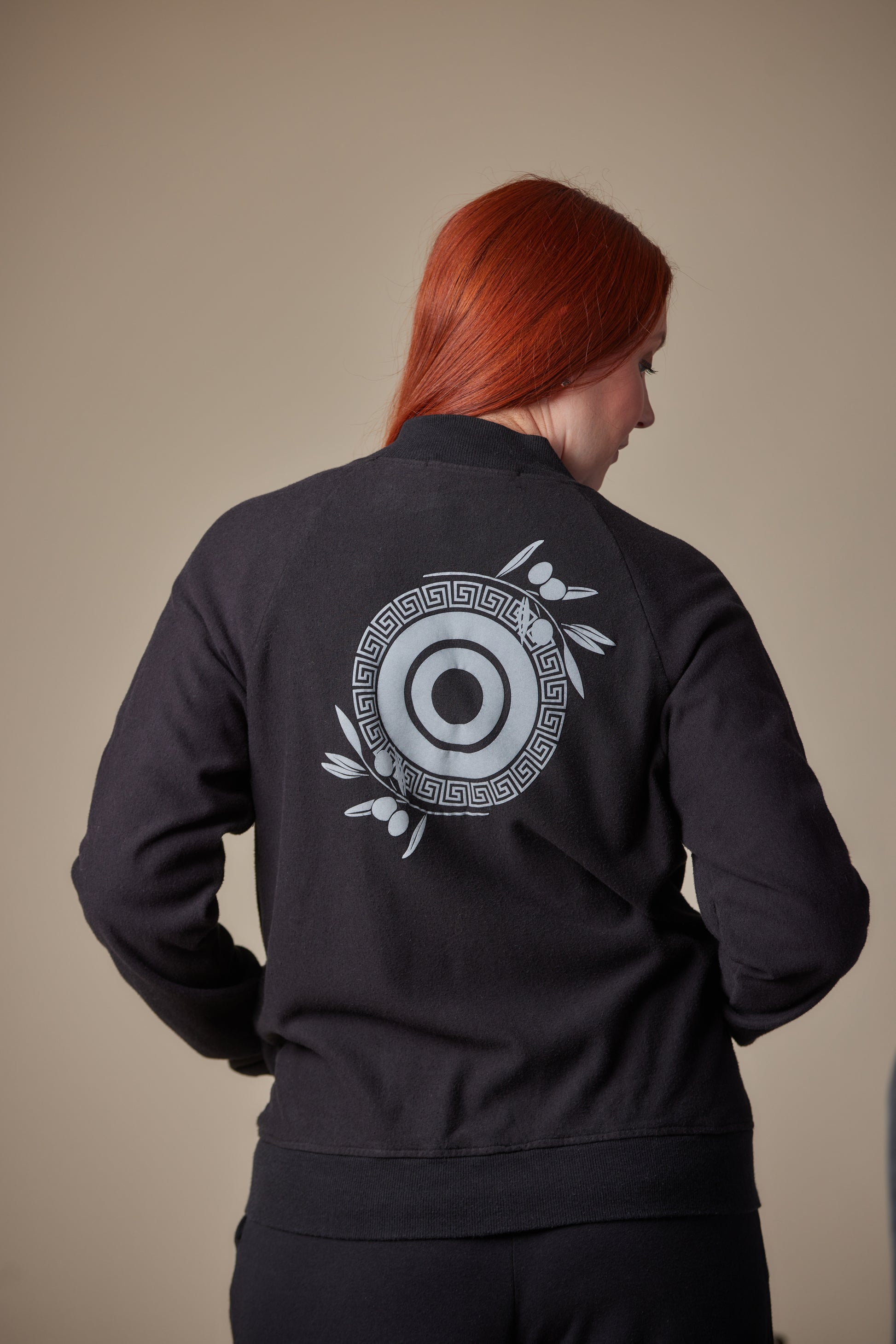 Person wearing a black jacket with a circular design on the back against a beige background