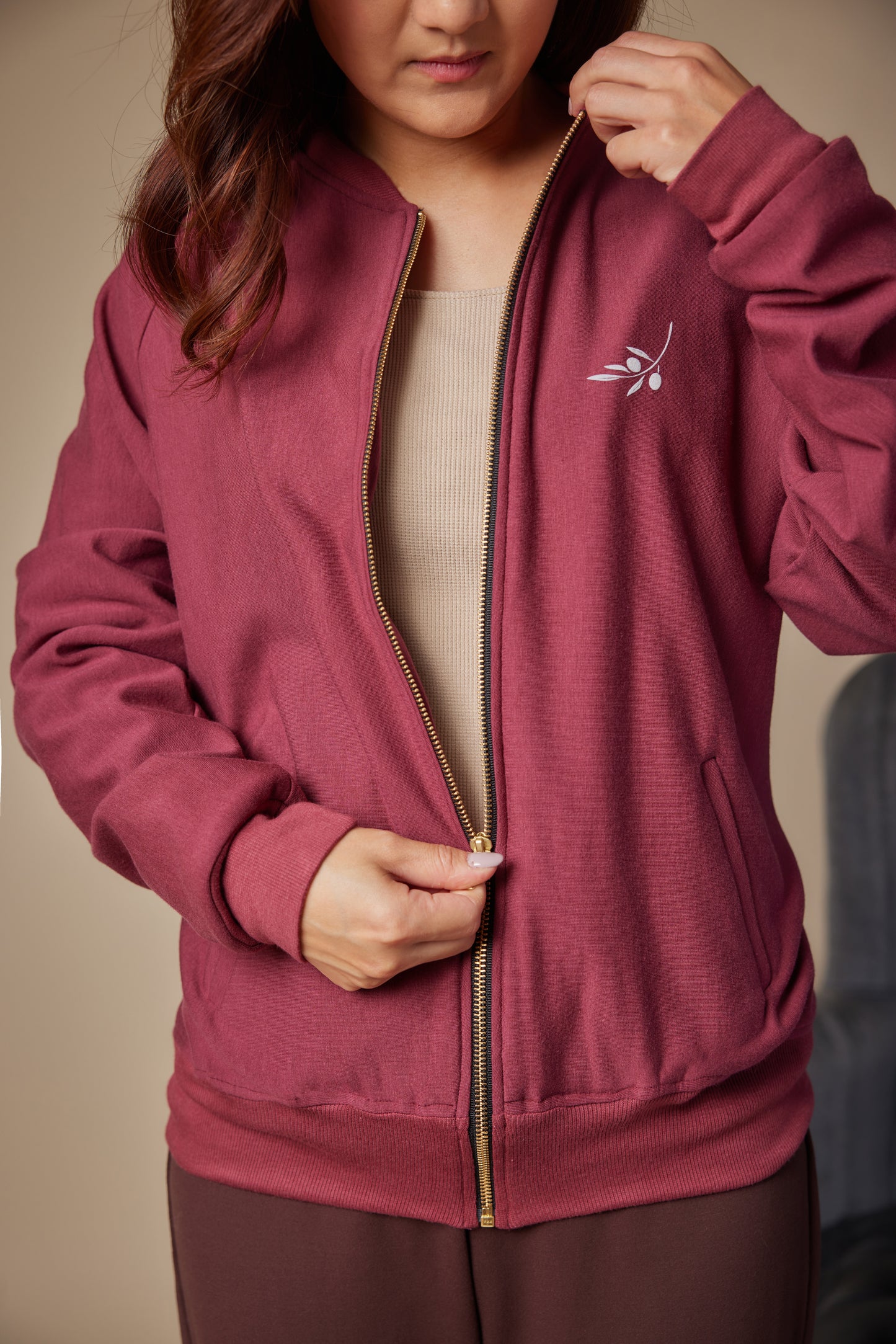 Person wearing a maroon zip-up hoodie with a logo on a beige background