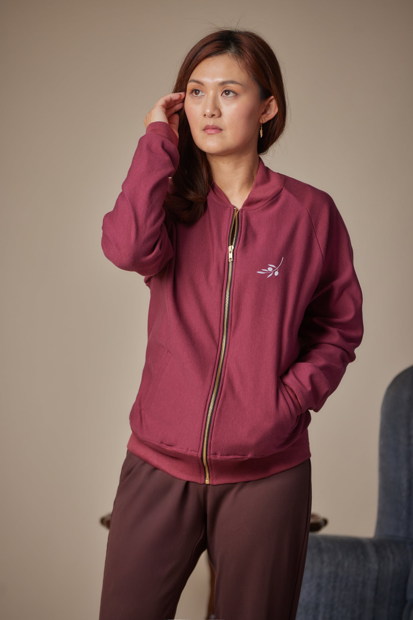 Woman wearing a maroon tracksuit with a logo on a beige background