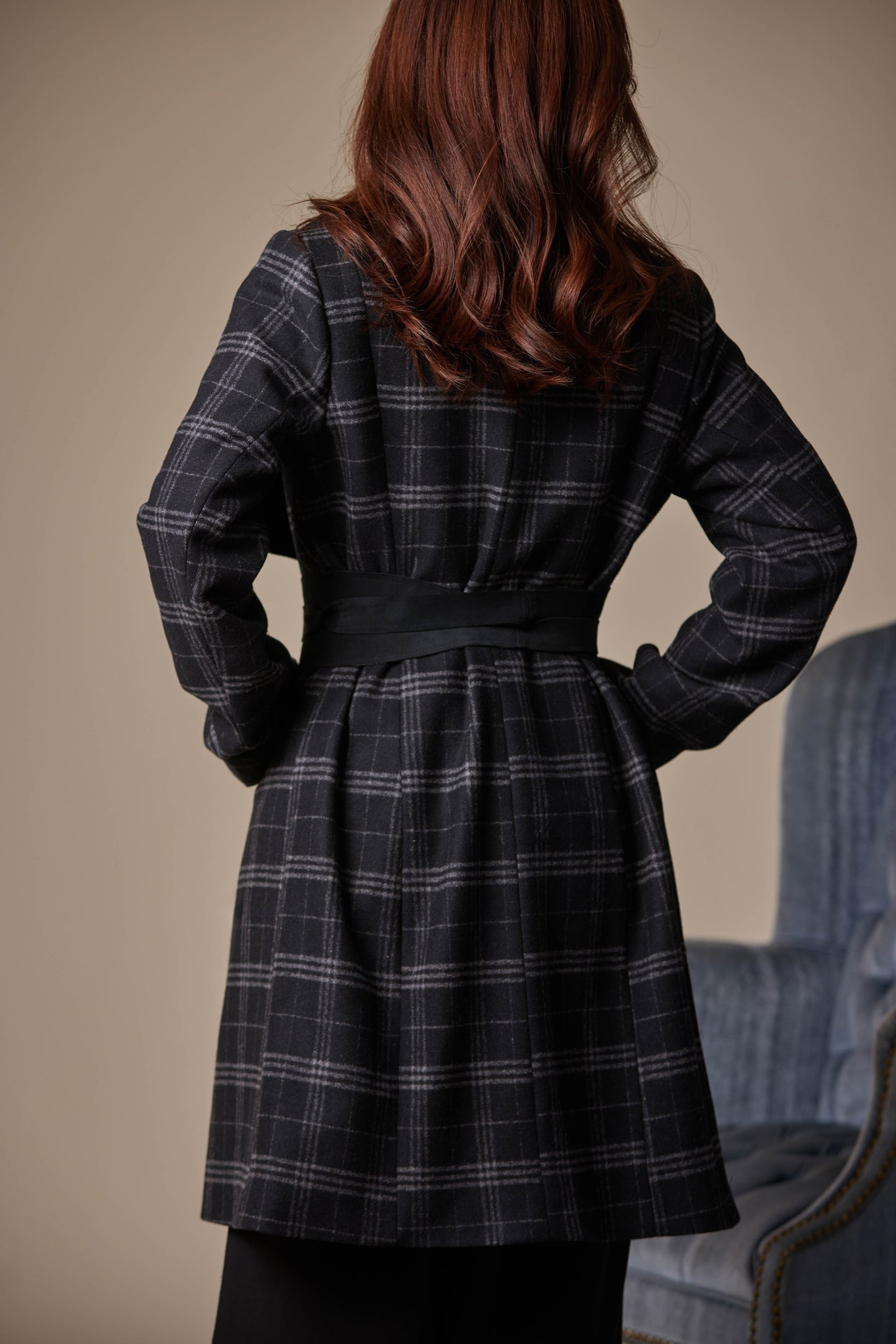 Person wearing a black plaid coat with hands on hips against a neutral background