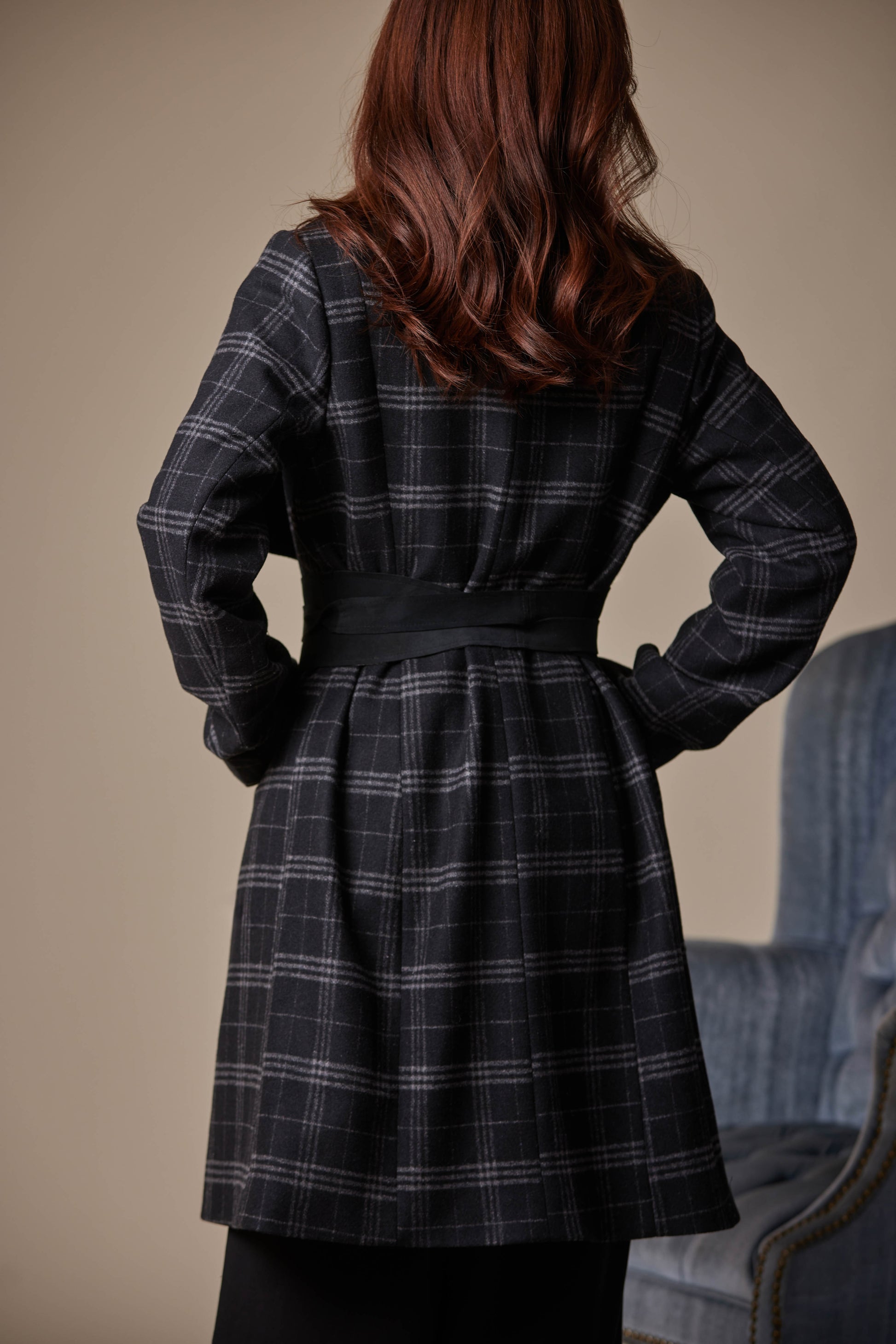 Person wearing a black plaid coat with hands on hips against a neutral background
