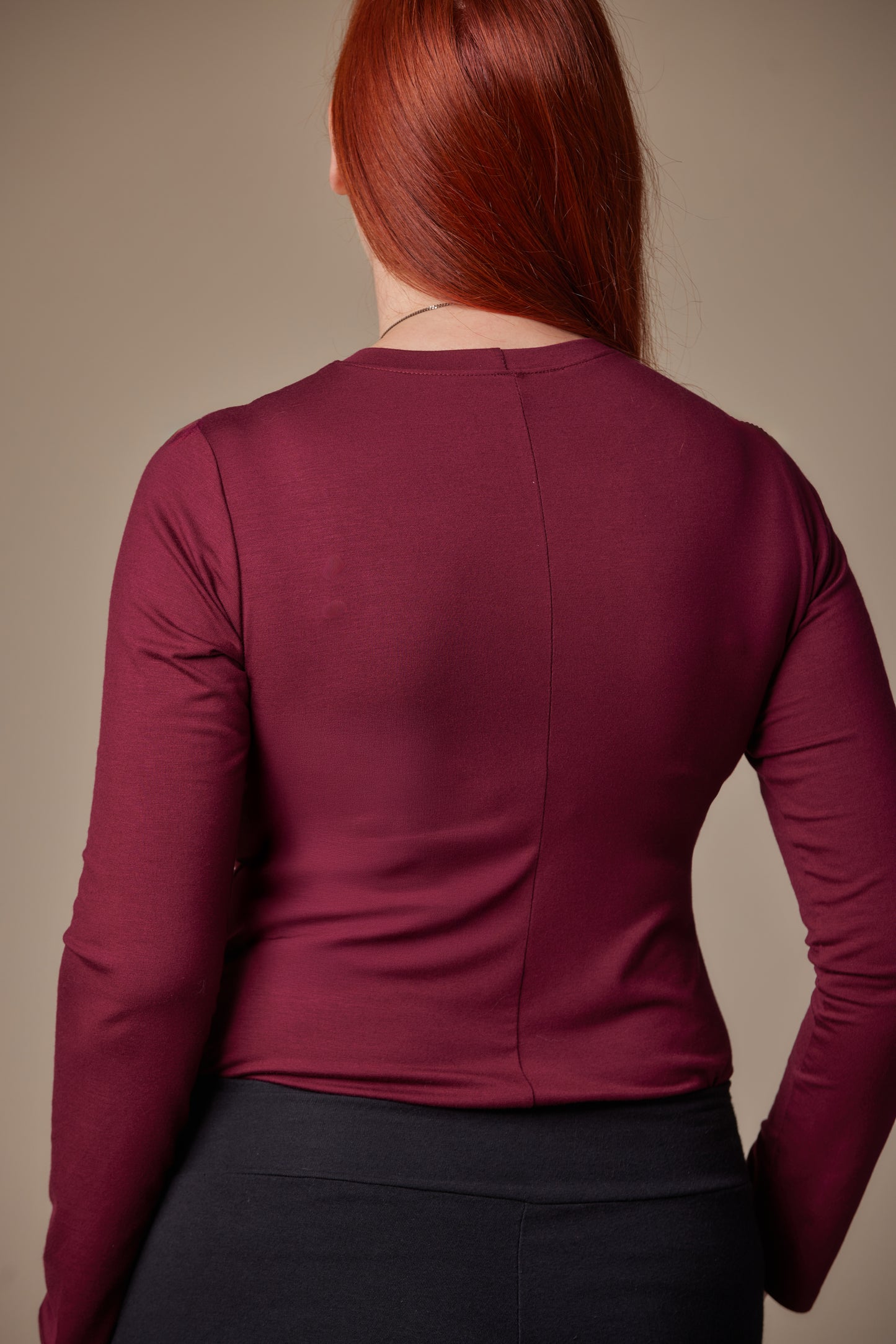 Person wearing a burgundy long-sleeve top against a beige background