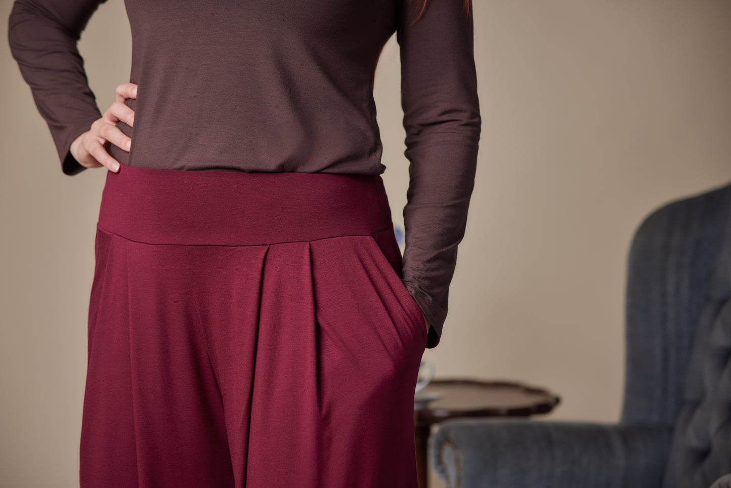 Person wearing a brown top and maroon pants against a neutral background