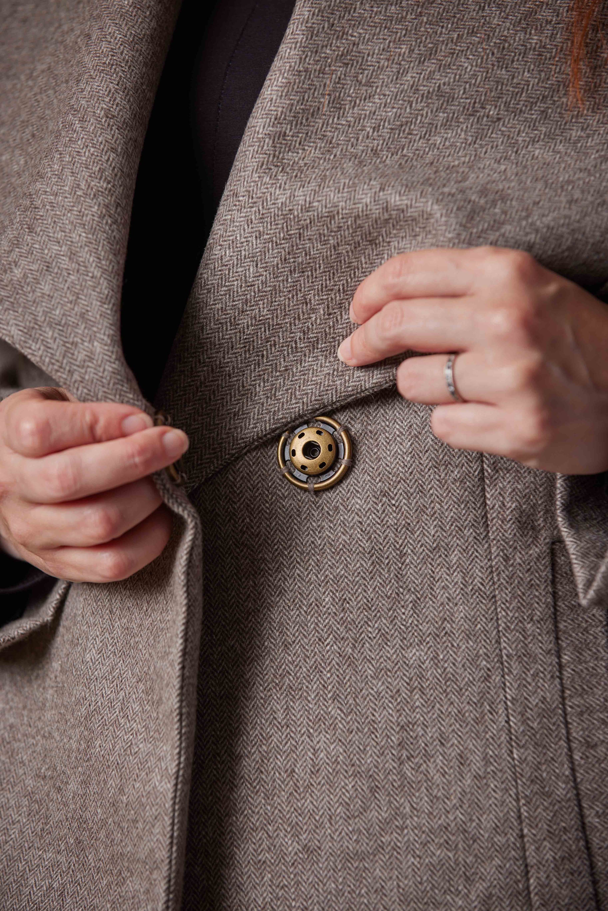 Close-up of a person buttoning a Brown coat with a focus on the button and fabric texture.