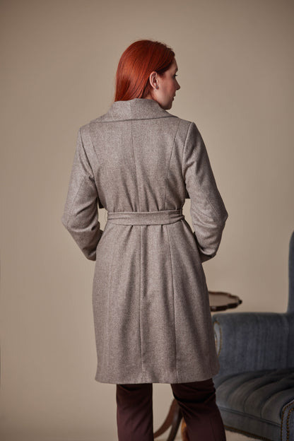 Person wearing a Brown coat standing in a room with a beige wall and a blue chair.