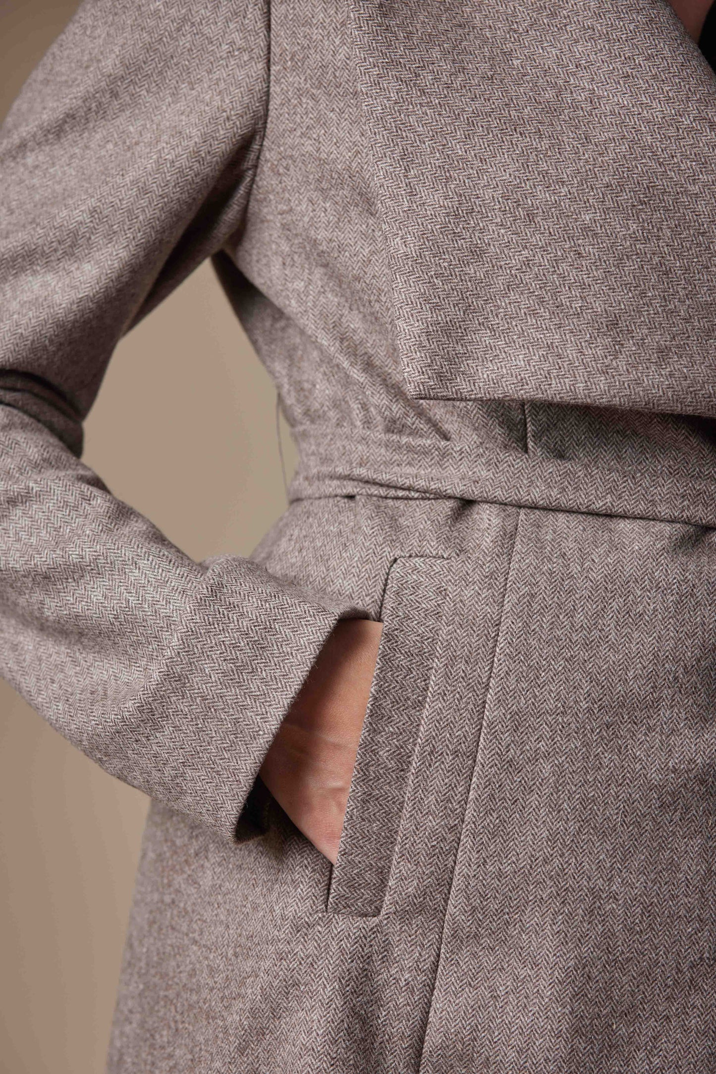 Close-up of a brown coat with a belt on a beige background