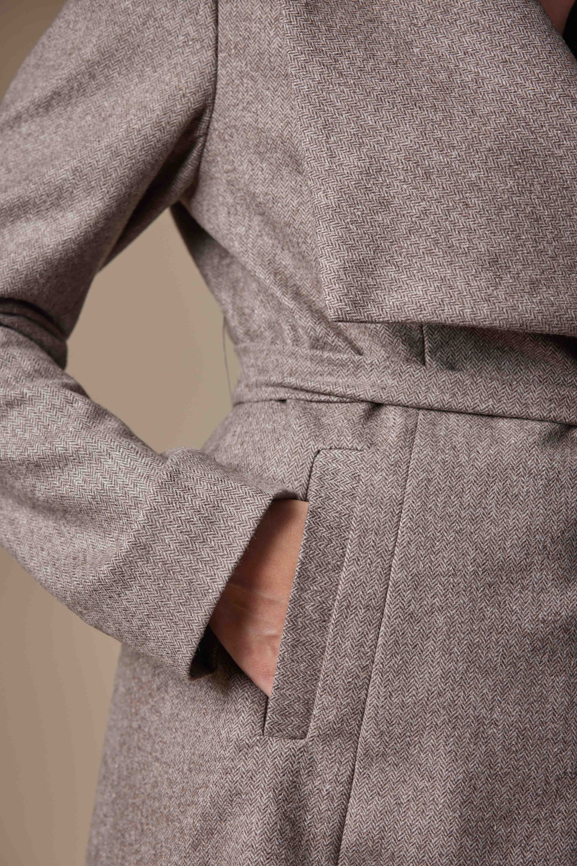 Close-up of a brown coat with a belt on a beige background