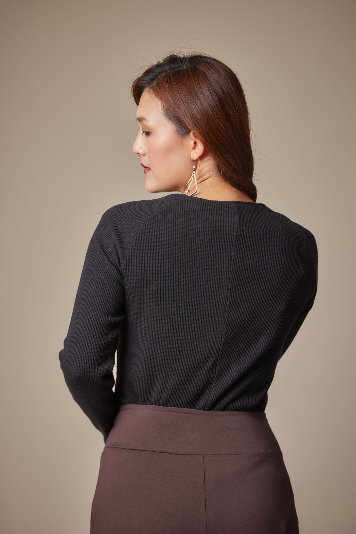 Woman wearing a black top and brown pants against a beige background