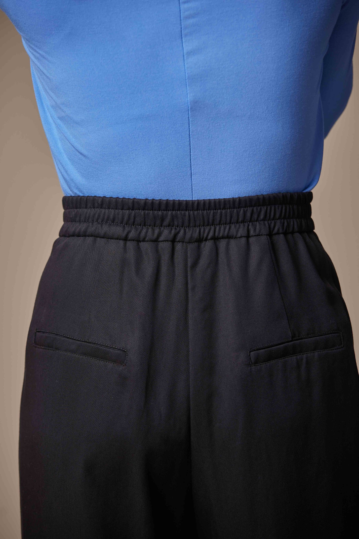 Person wearing a blue shirt and black pants against a beige background