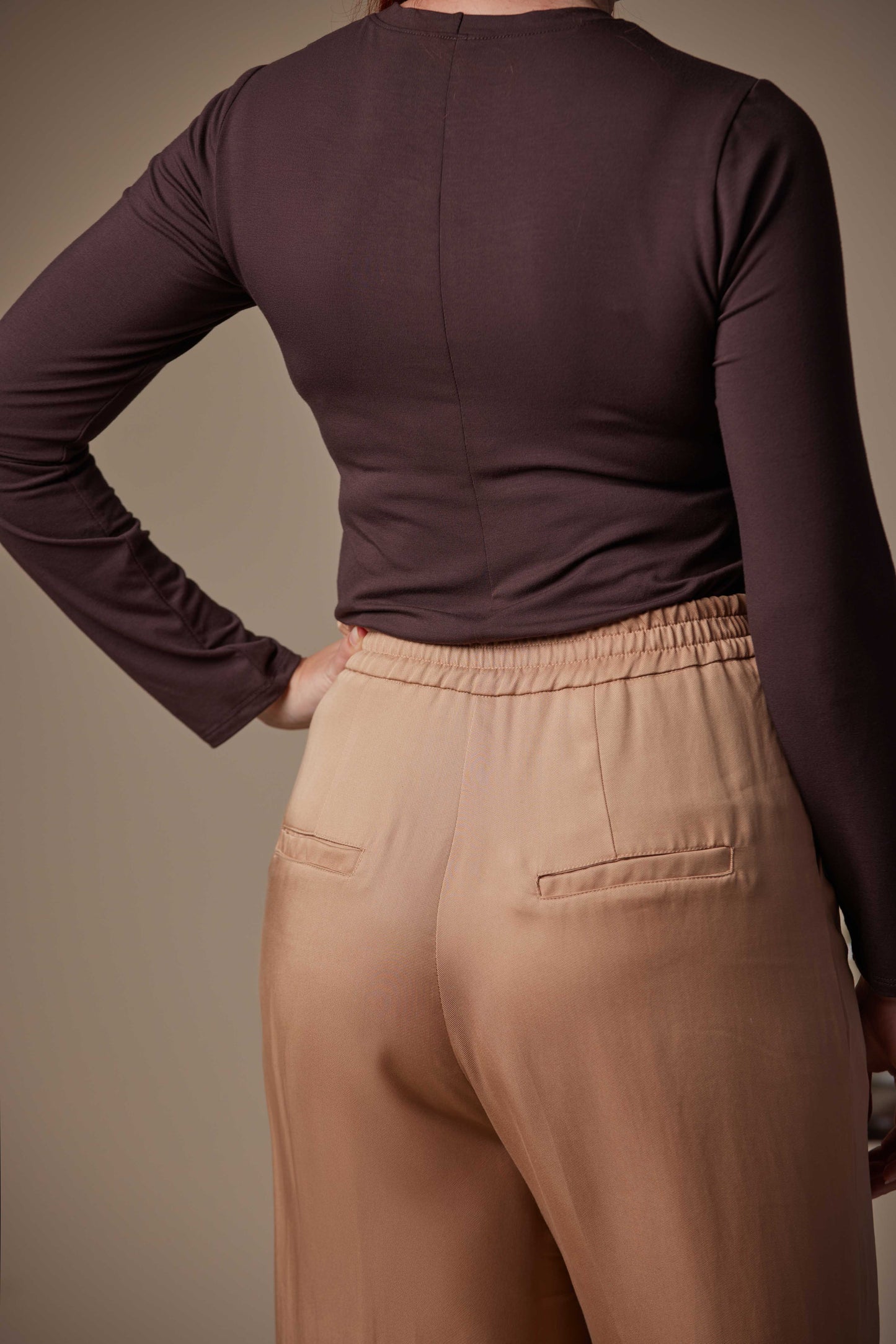 Person wearing a brown long-sleeve top and beige pants against a neutral background