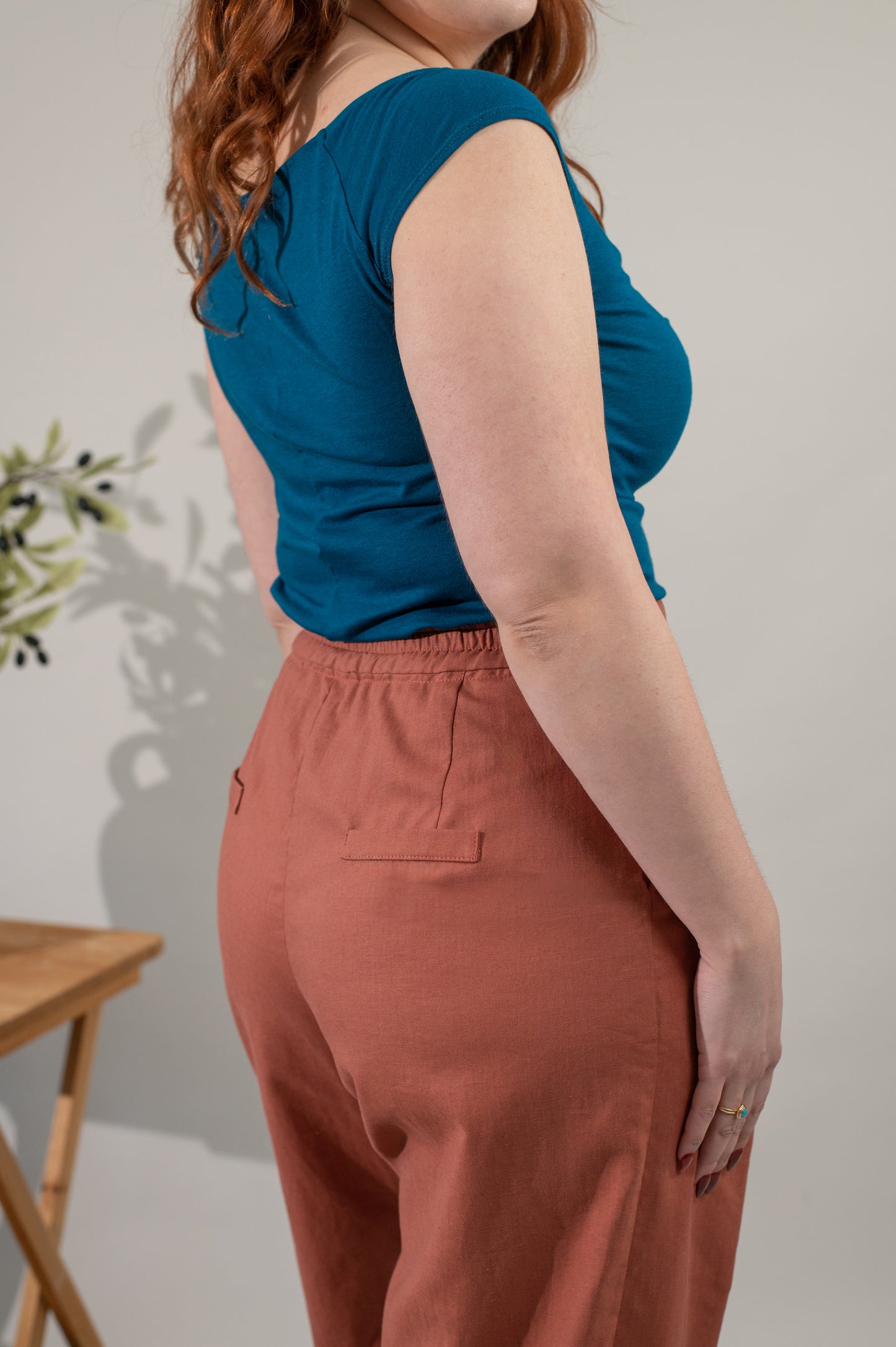 Person wearing a blue sleeveless top and brown pants against a neutral background