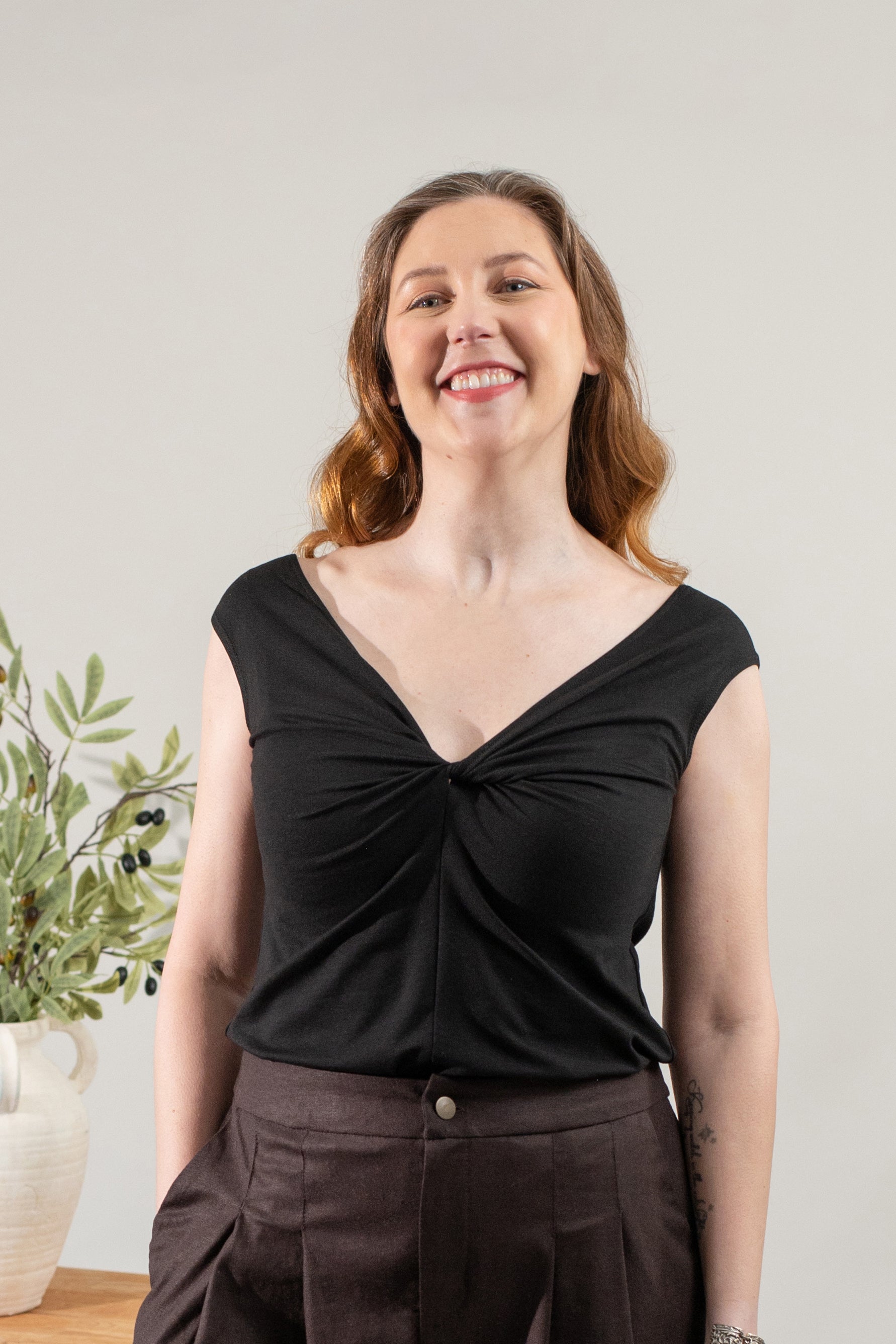 Woman wearing a black top and brown pants standing indoors with a neutral background