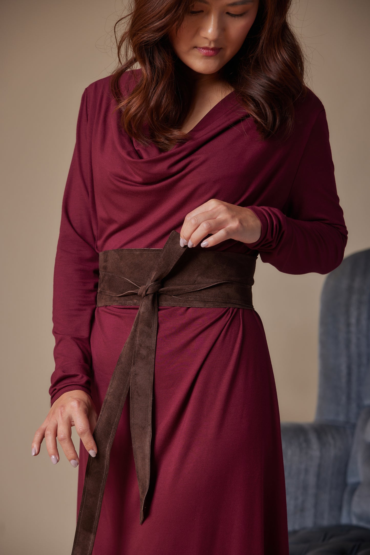 Woman wearing a burgundy dress with a brown belt against a neutral background