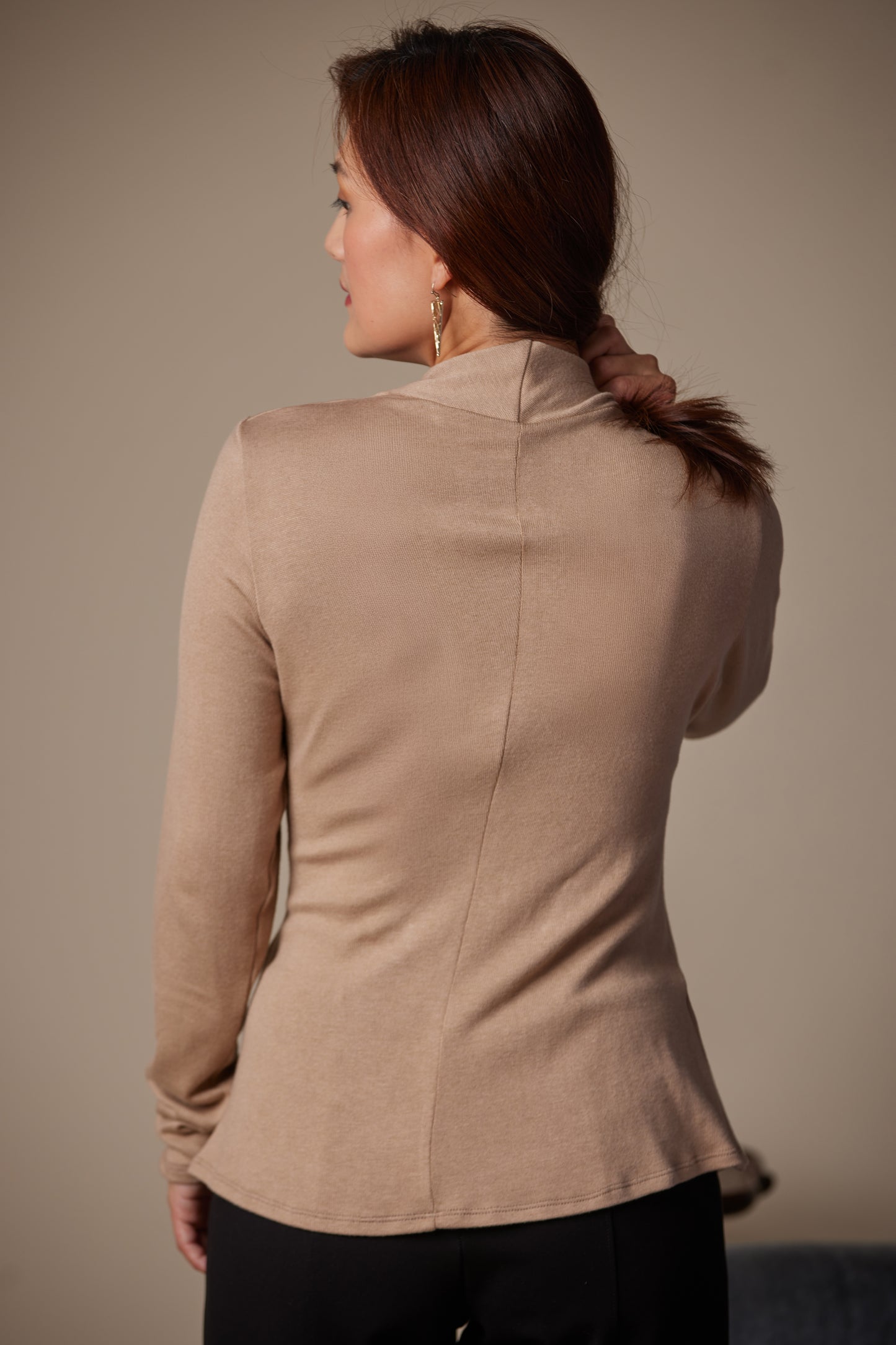 Woman wearing a beige long-sleeve top against a plain background