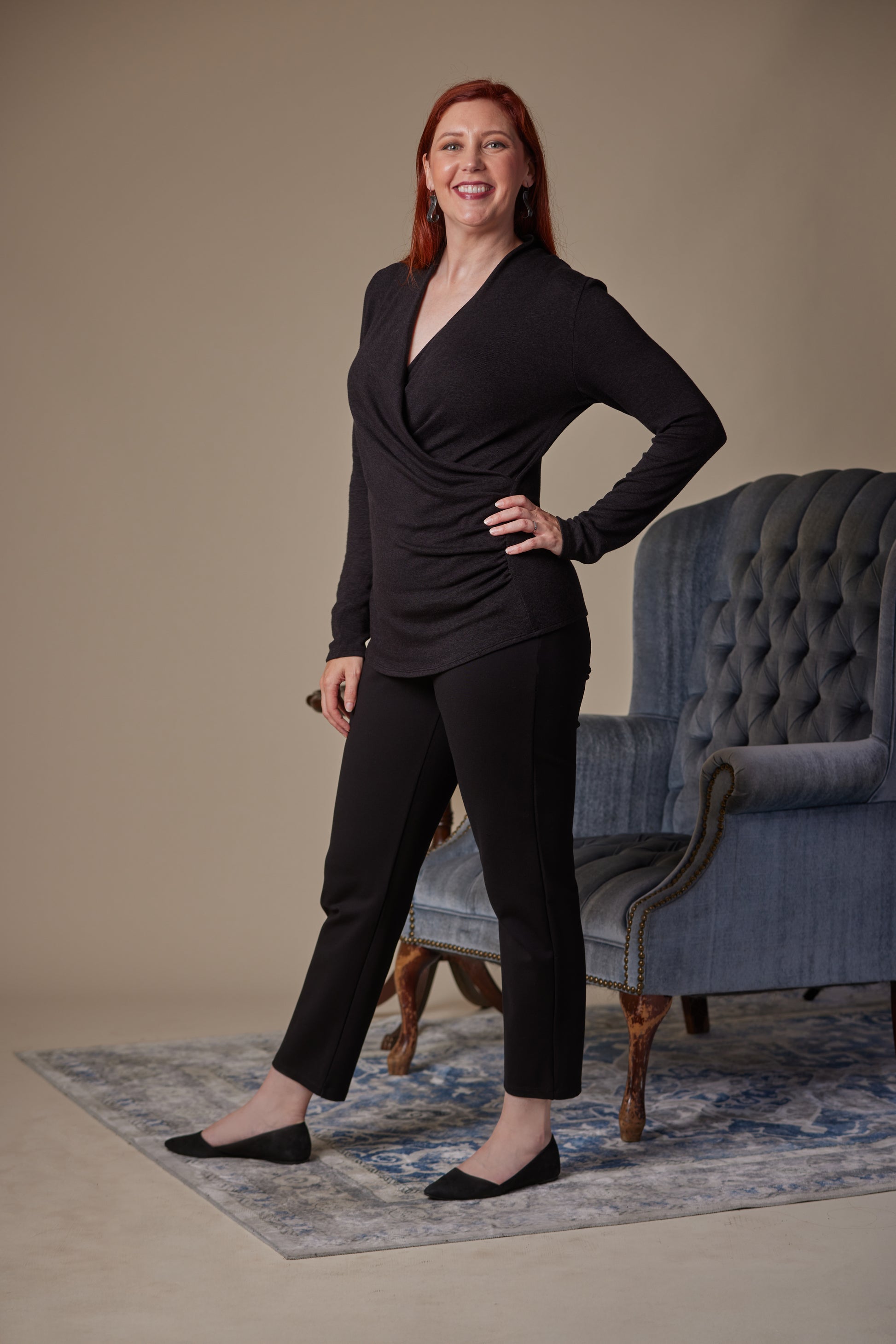 Woman in a black outfit standing in a room with a blue armchair.
