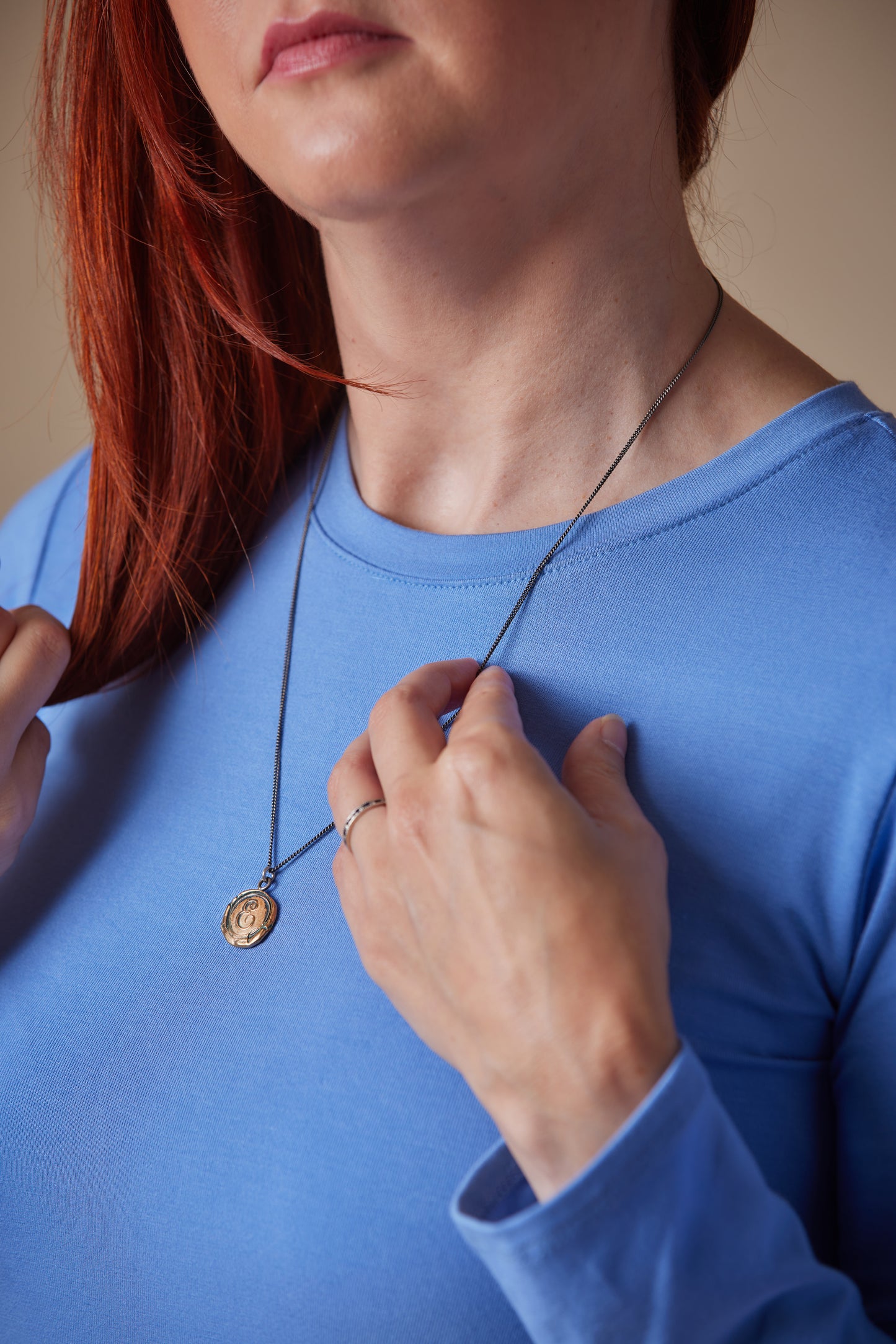 Person wearing a blue shirt and holding a necklace with a pendant.