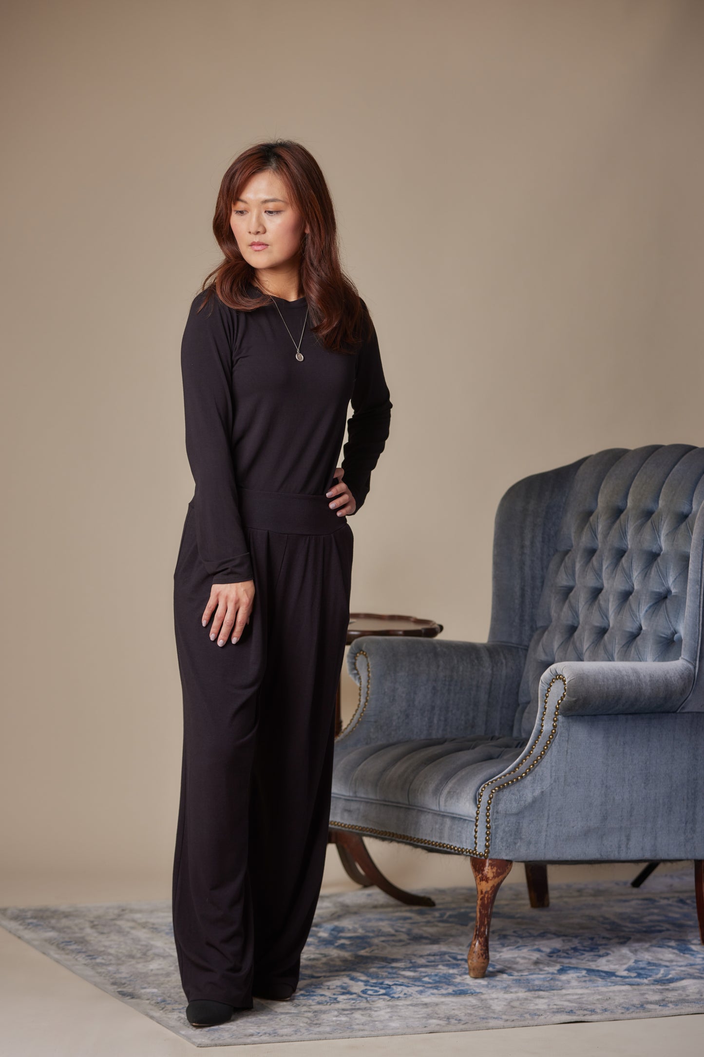 Woman in a black outfit standing in a room with a blue armchair.