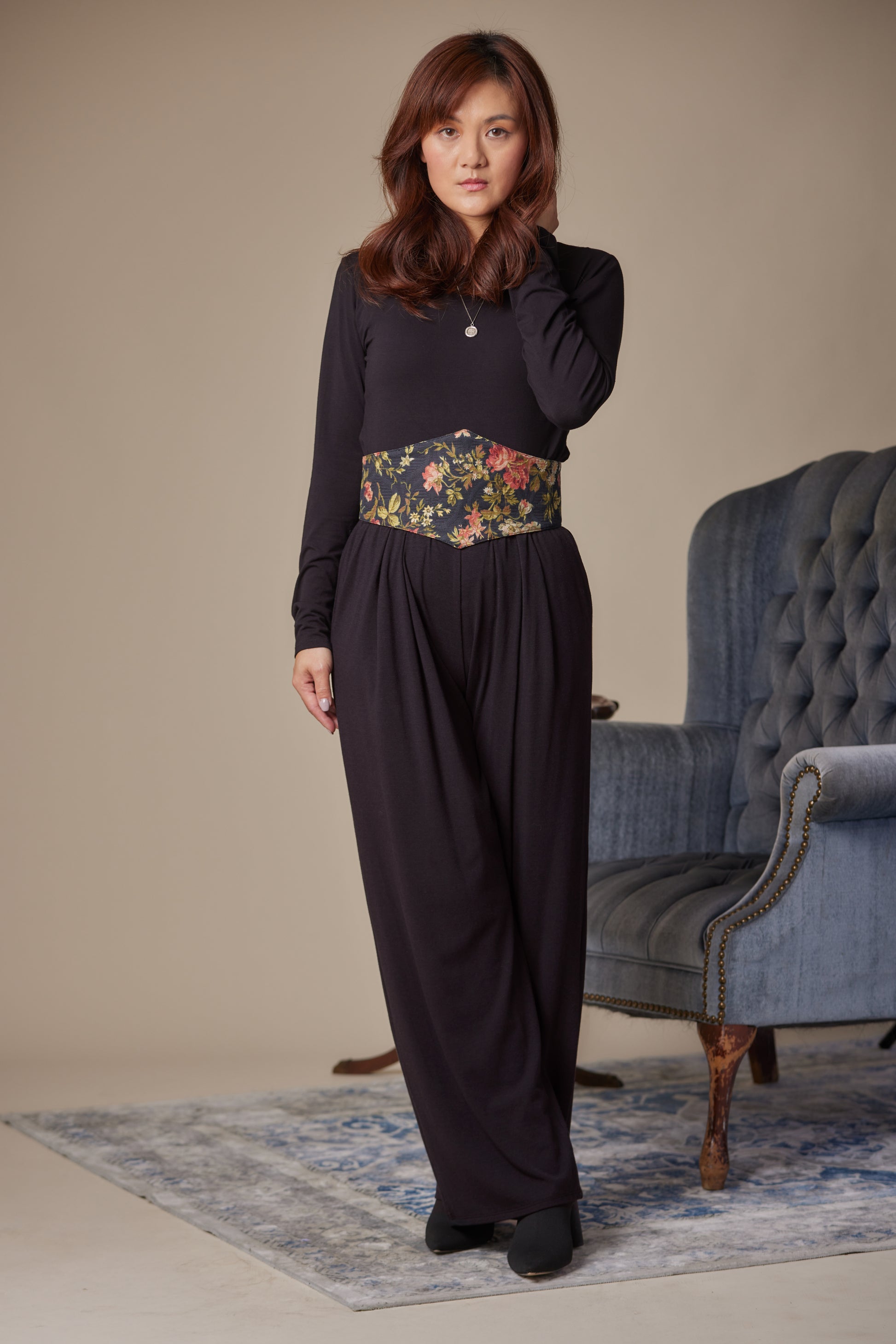 Woman wearing a dark outfit with a floral belt in a room with a blue armchair.