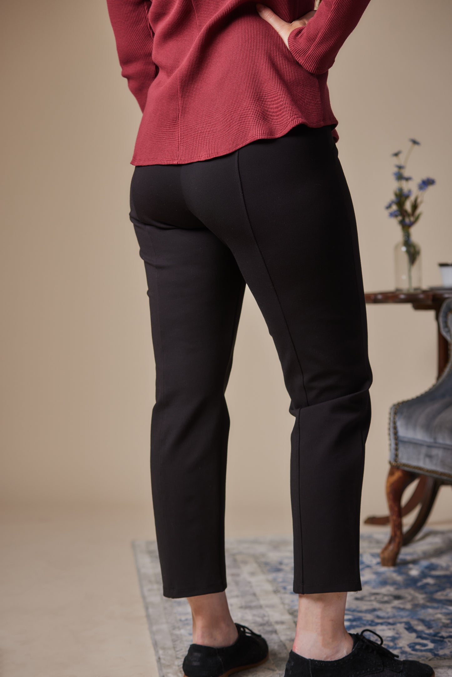 Person wearing black pants and a red top in a room with a table and flowers.