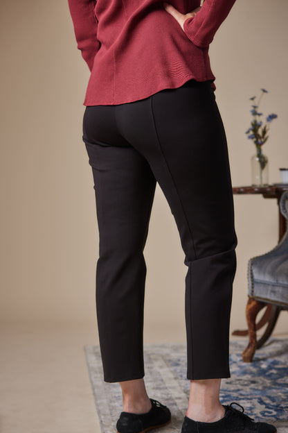 Person wearing black pants and a red top in a room with a table and flowers.