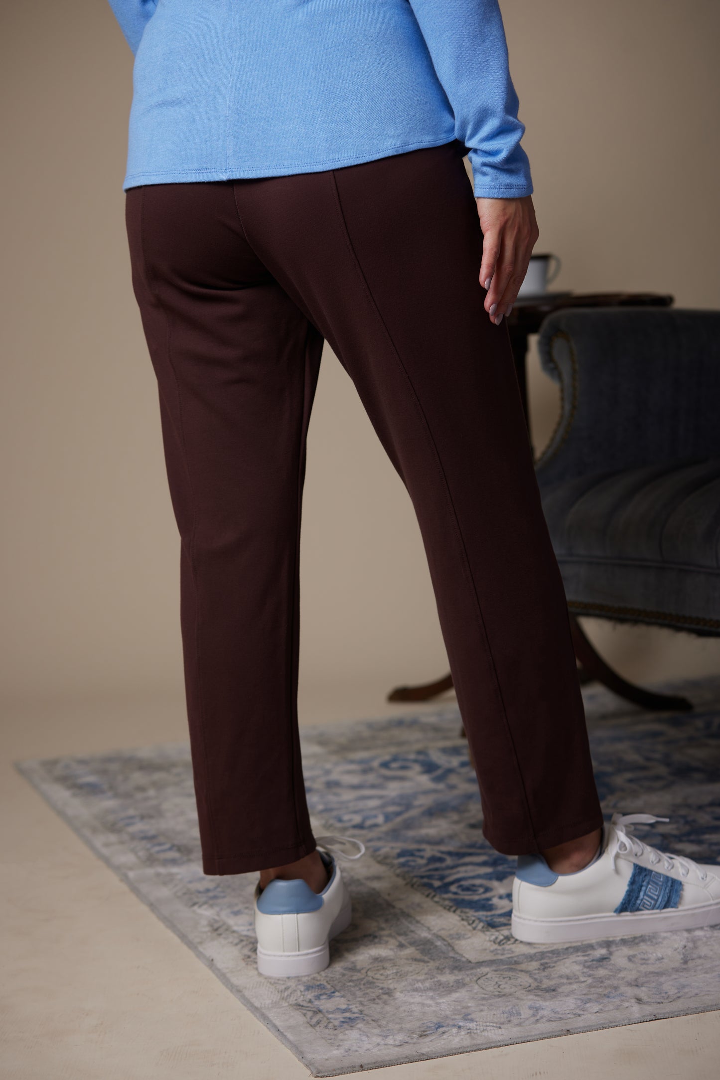 Person wearing brown pants and blue shirt standing on a patterned rug.