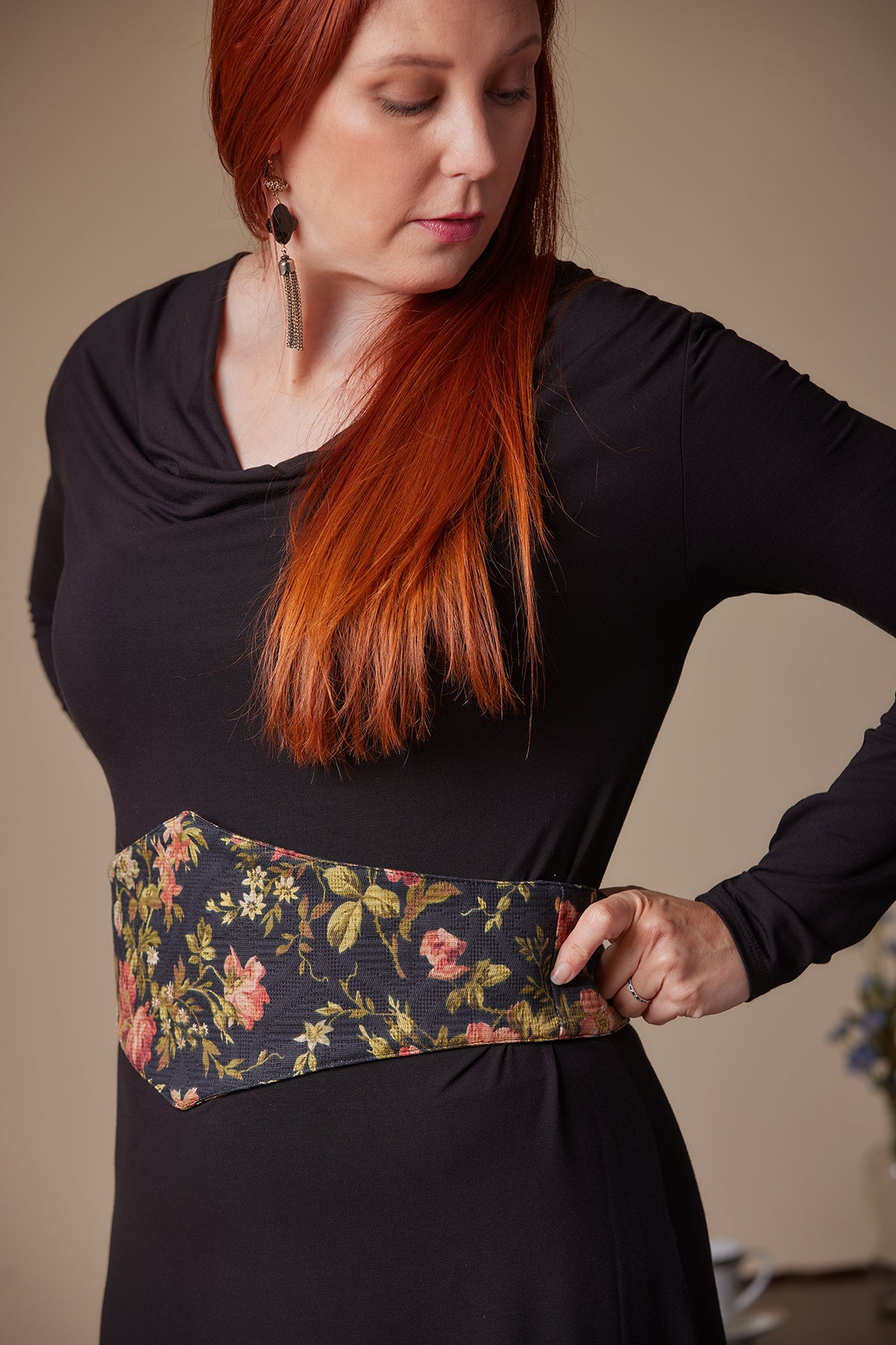 Woman wearing a black top with a floral belt against a neutral background