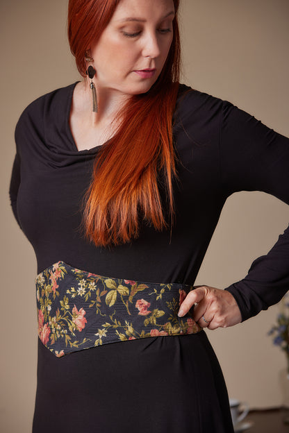 Woman wearing a black top with a floral belt against a neutral background