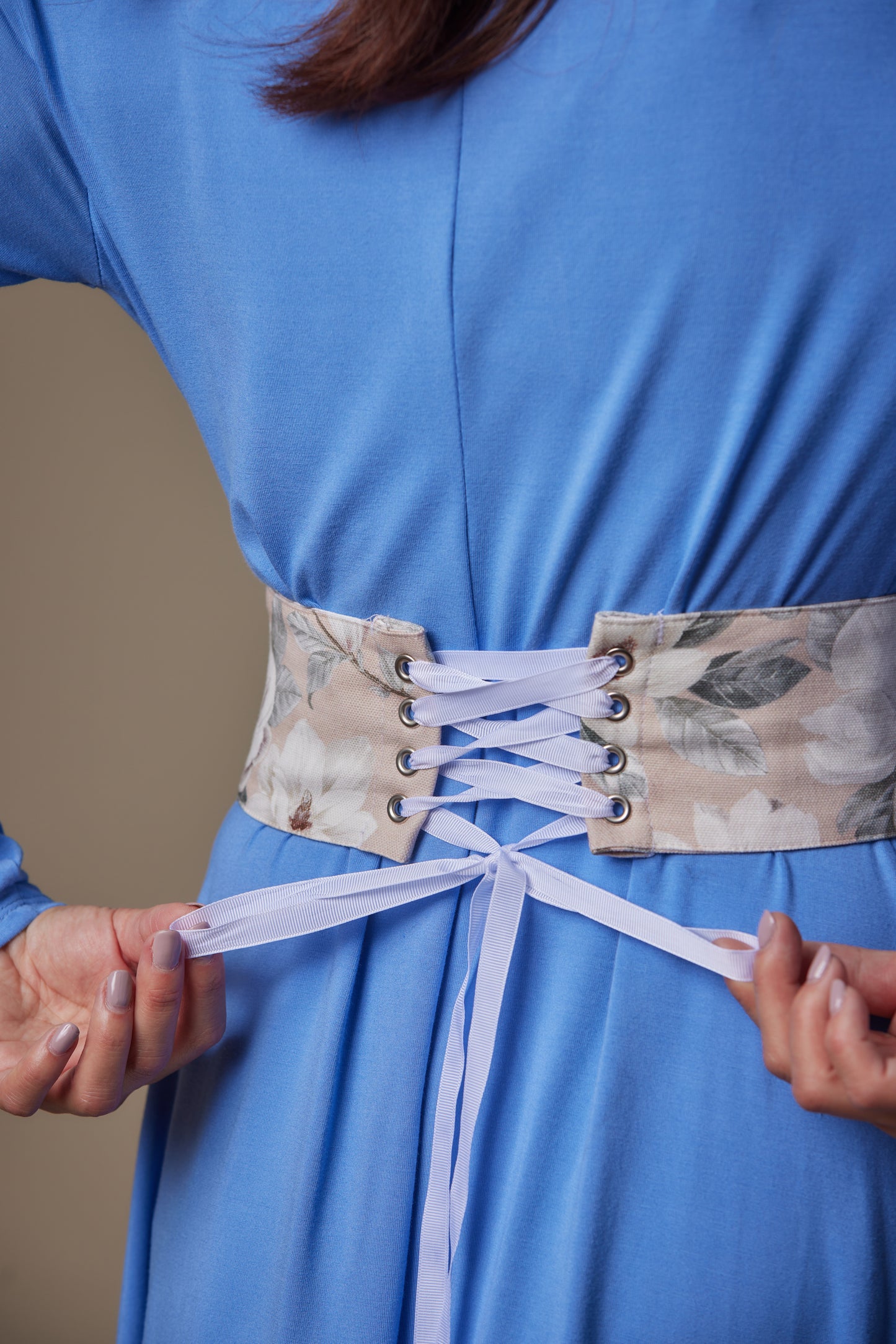 Person wearing a blue dress with a floral corset belt, focusing on the waist area.