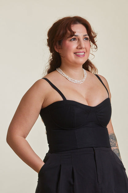 Woman wearing a black sleeveless top and shorts standing in a room with wooden chairs.