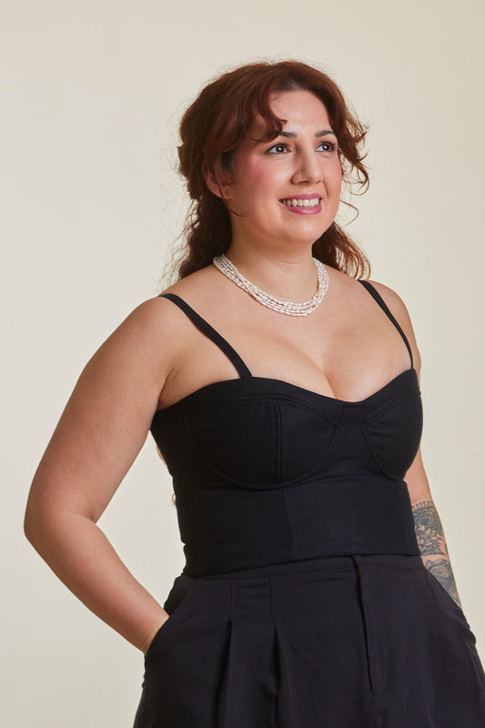 Woman wearing a black sleeveless top and shorts standing in a room with wooden chairs.