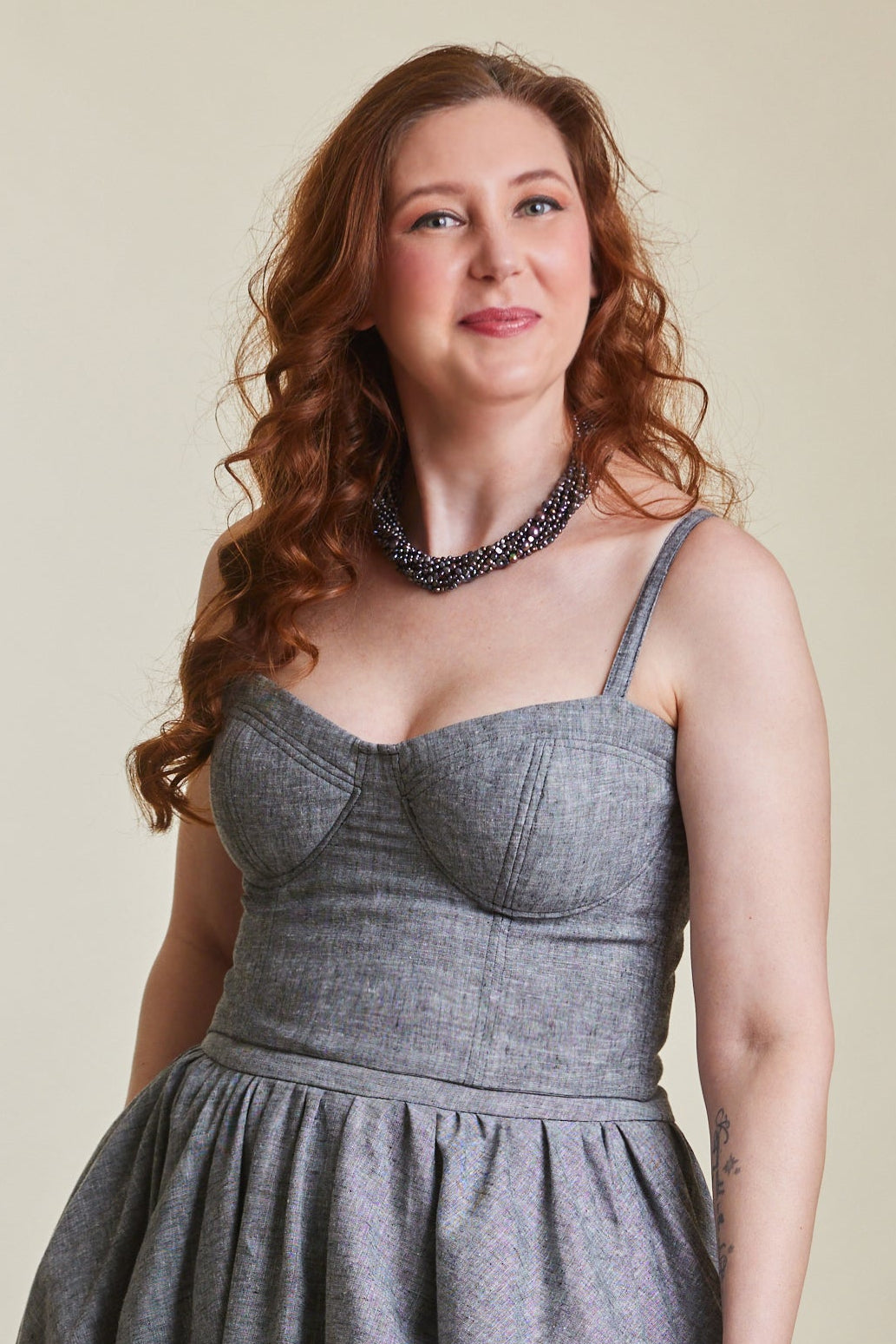 Woman wearing a gray dress standing in a room with a chair and table.