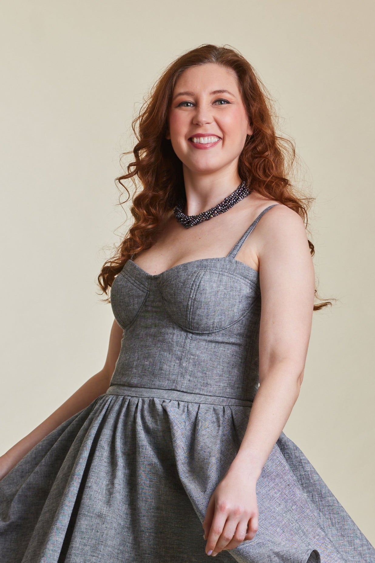 Woman wearing a gray dress with a subtle pattern, standing against a plain background.