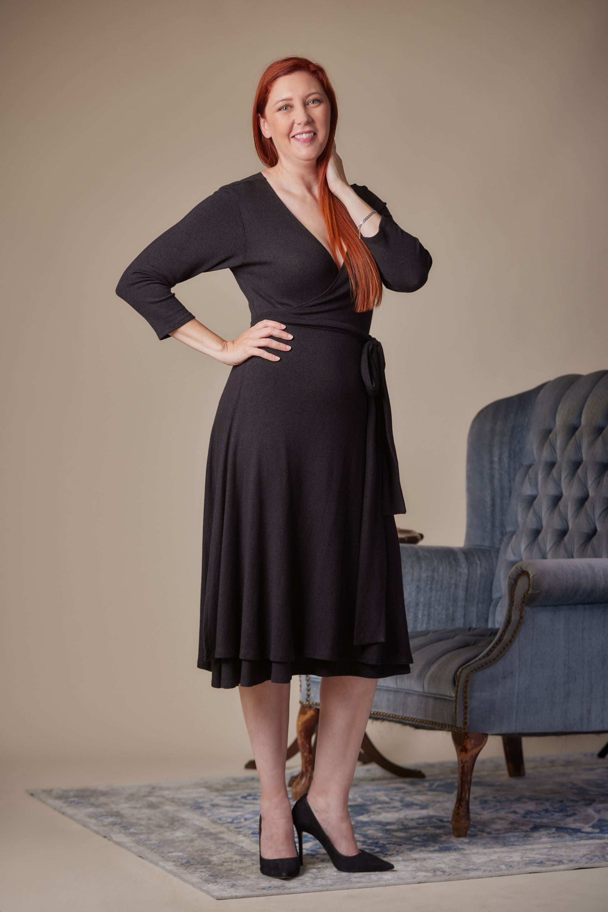 Woman wearing a black dress standing in a room with a blue armchair.