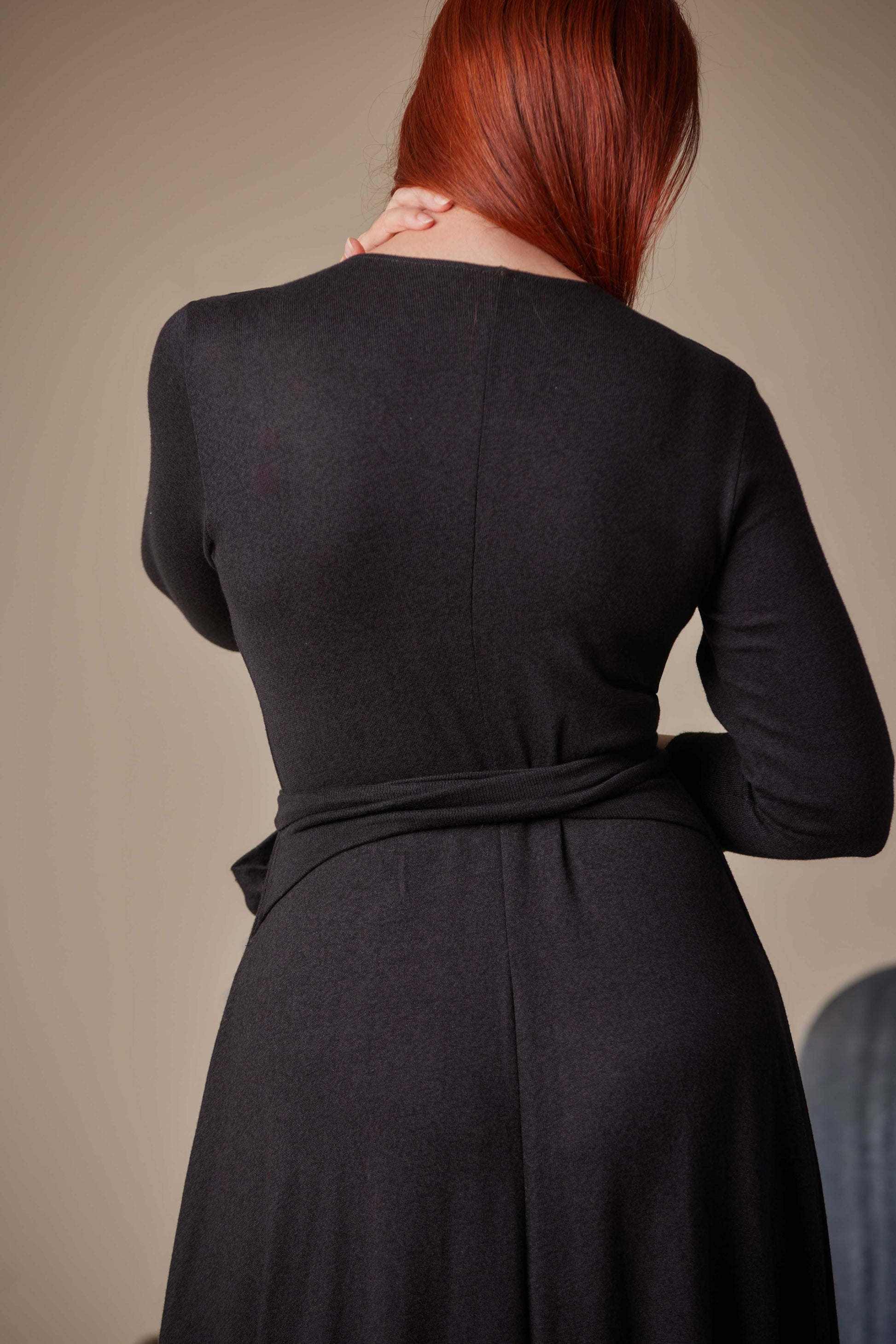 Person wearing a black dress with a belt against a beige background