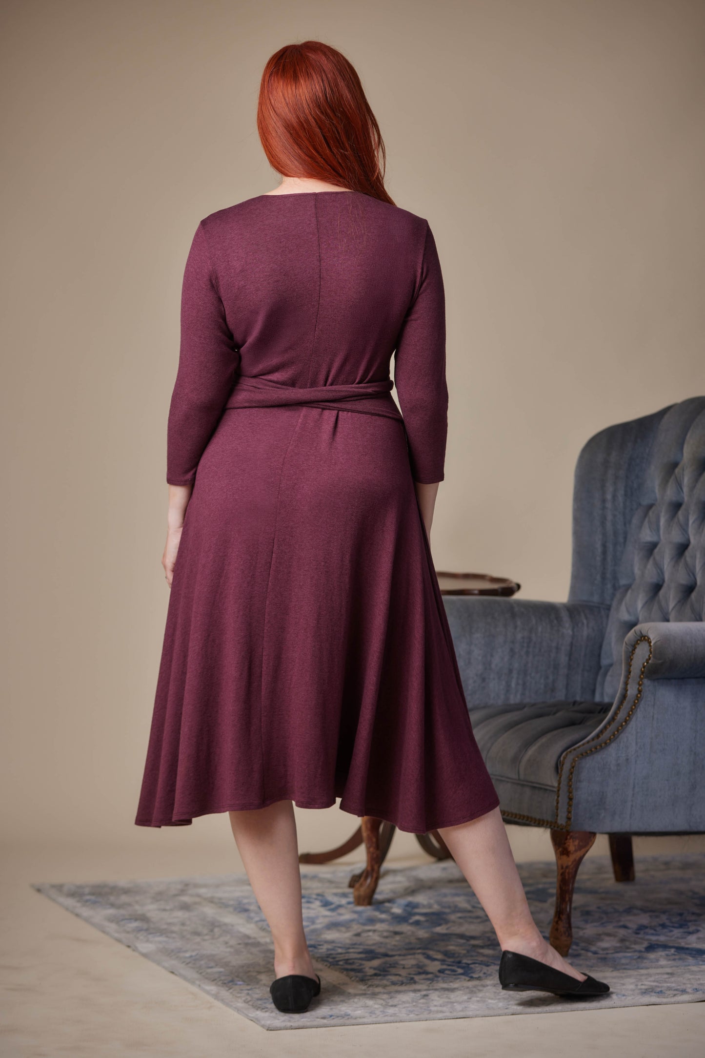 Woman wearing a purple dress standing in a room with a blue armchair.