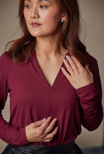 Woman wearing a burgundy long-sleeve top against a neutral background