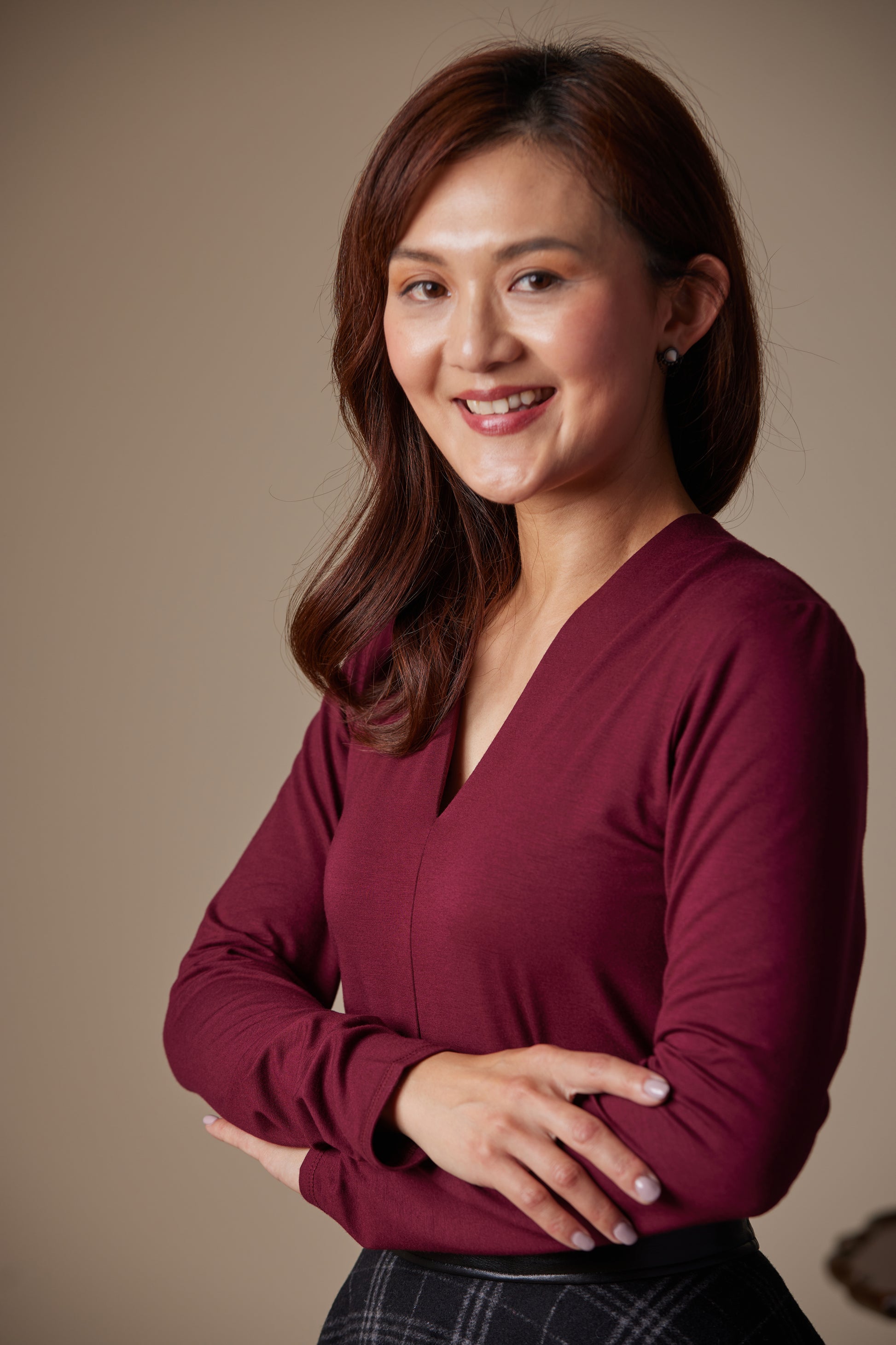 Woman wearing a maroon long-sleeve top against a beige background