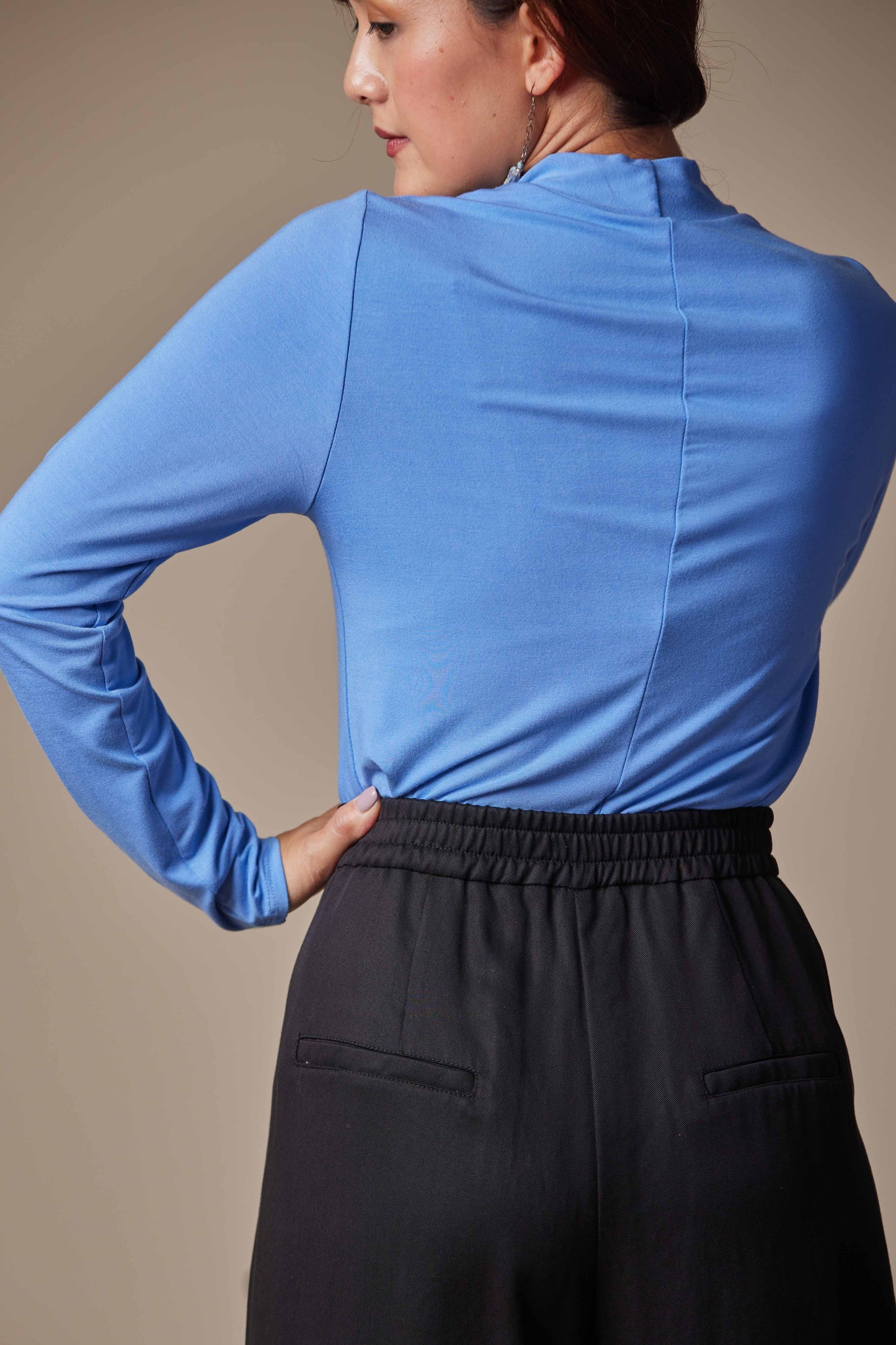 Person wearing a blue long-sleeve top and black pants against a beige background