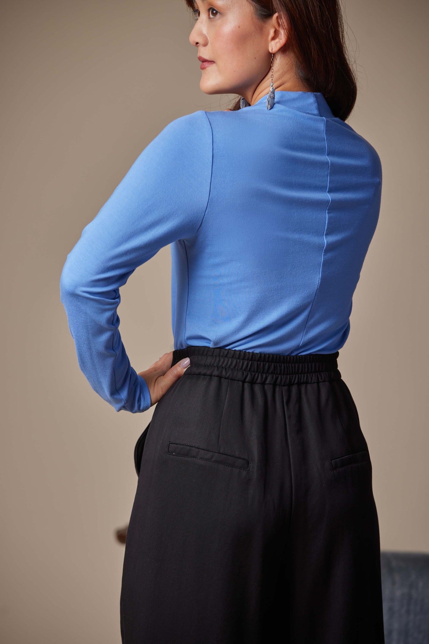 Woman wearing a blue long-sleeve top and black pants against a beige background