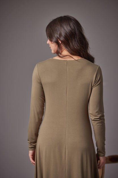A woman viewed from the back wearing a long-sleeve, knee-length knit dress in a muted fern color against a solid gray studio background.